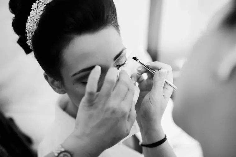 Black-and-white close-up of the bride's eye make-up being applied beneath her tiara