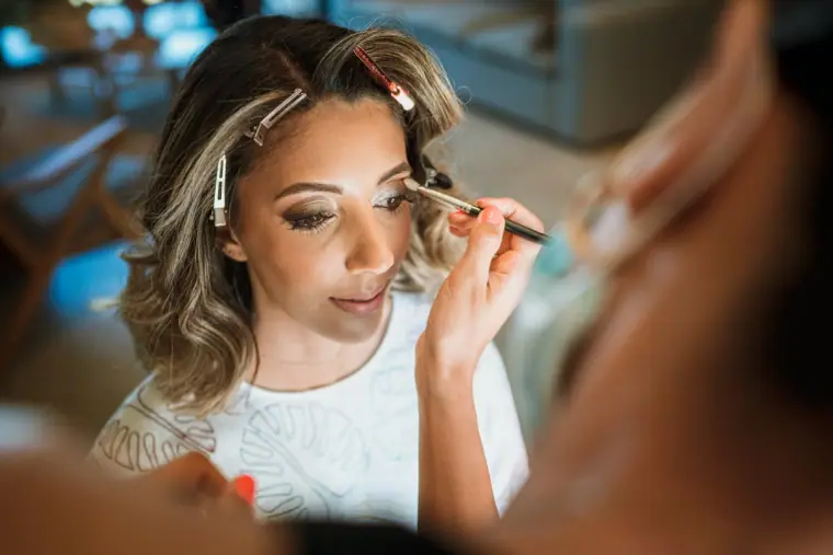 Bride having her eye make-up applied, hair clipped back, while getting ready
