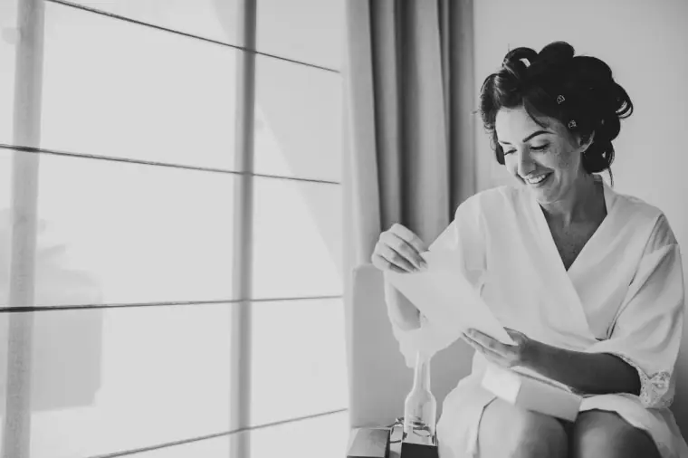 Black-and-white photo of Jaclyn in a robe and hair rollers, smiling as she reads a note