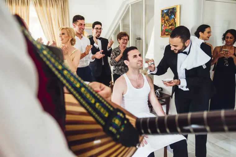 Best man shaving Angelos as musicians play and family look on