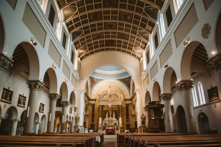 Interior of a church with a coffered barrel-vaulted ceiling, arches and rows of pews
