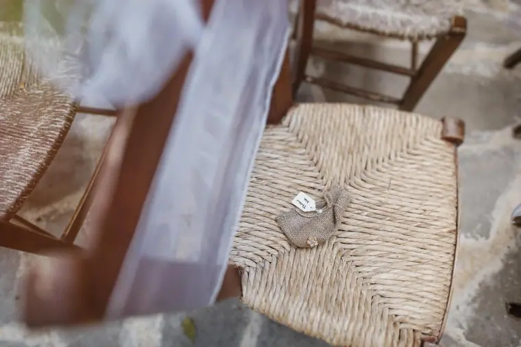 Ring box resting on a rush-seated chair beside a ribbon-tied aisle