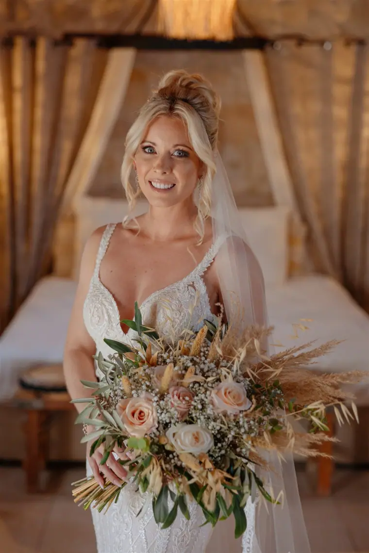 Sarah smiling with her boho bouquet in the warmly lit suite