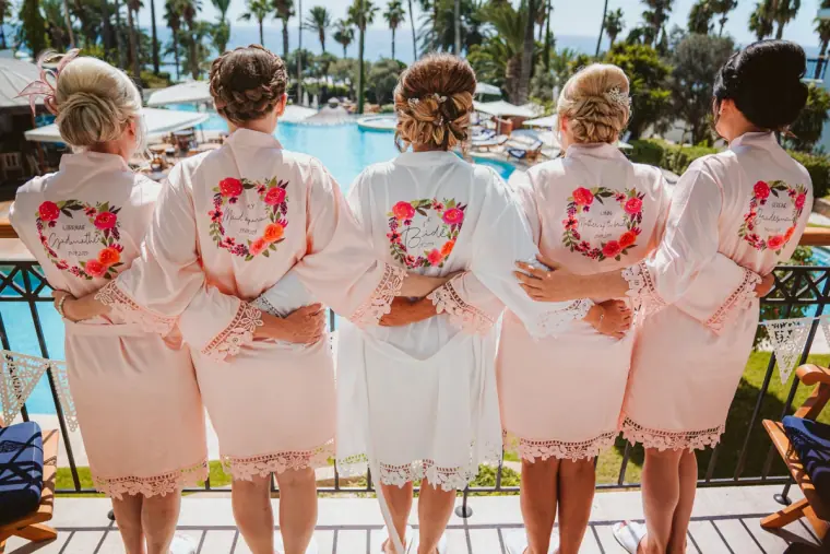 Bride and bridesmaids from behind in personalised floral robes, arms around each other