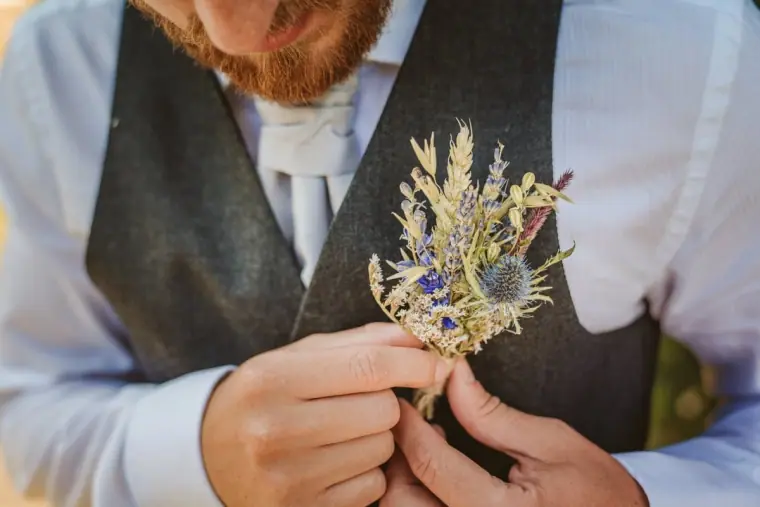 Groom pinning a thistle and dried-flower buttonhole to his tweed waistcoat
