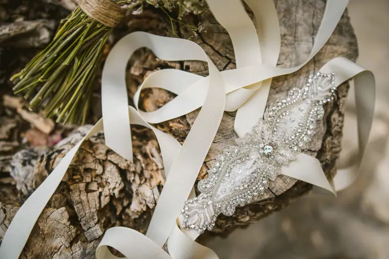 Bouquet stems and a jewelled bridal belt with ivory ribbon on rough bark