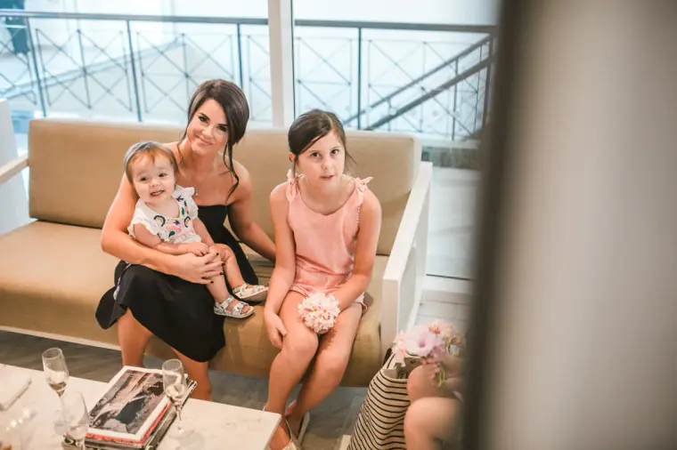 Woman on a sofa with a baby and a little girl in pink while the bride gets ready