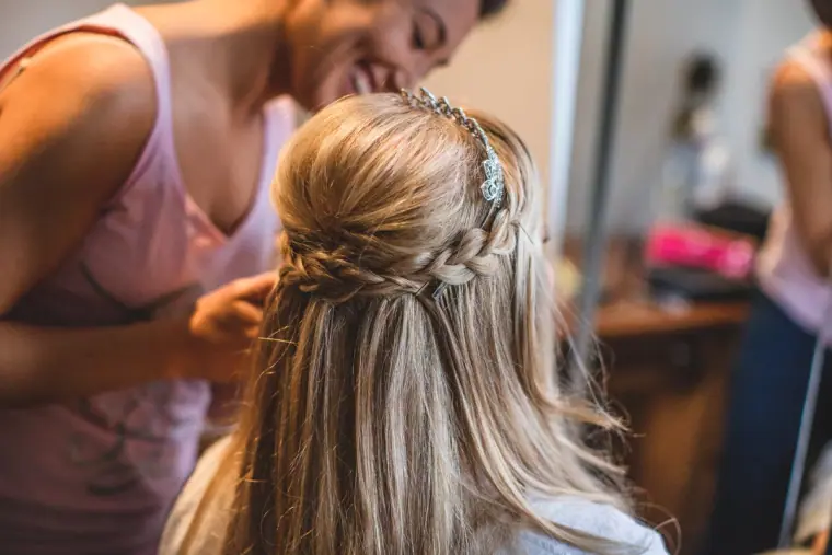 Hairdresser pinning a braided half-up style with a sparkling headband for the bride