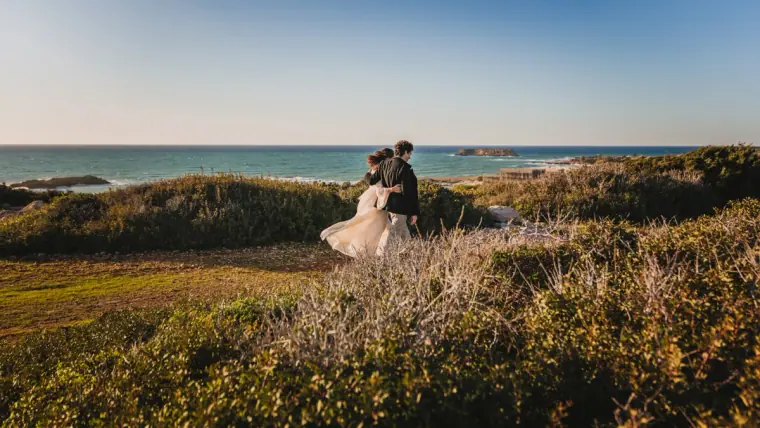 Couple standing in wild grasses on the clifftop with the sea on the horizon