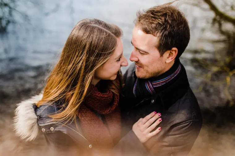 Couple smiling nose to nose in winter coats beside the lake