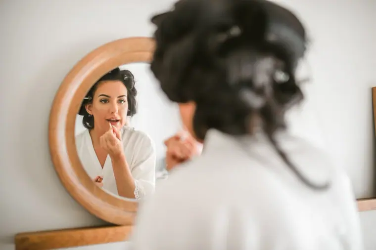 Jaclyn applying lipstick in a round wooden mirror, hair pinned up in curls