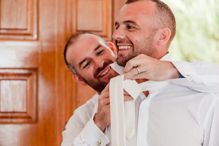 Friend helping the groom with his tie in front of a wooden door