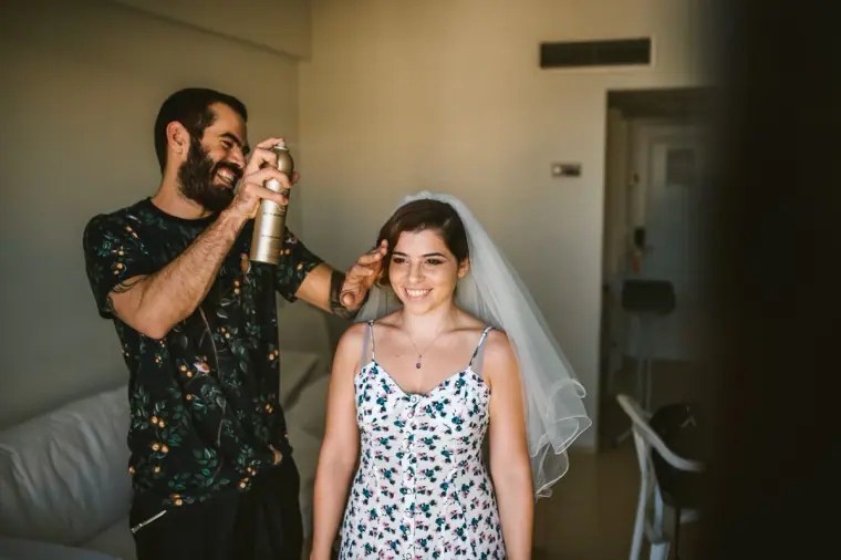 Hairdresser spraying the bride's hair as she smiles in her veil