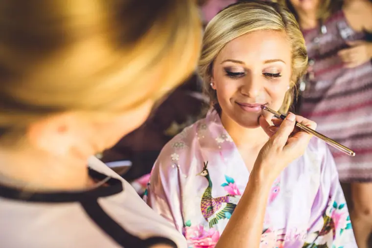 Bride in a floral robe having lipstick applied by the make-up artist