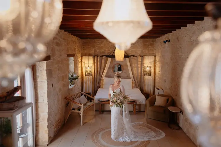 Bride in her gown beneath a chandelier in the stone-walled suite at Liopetro