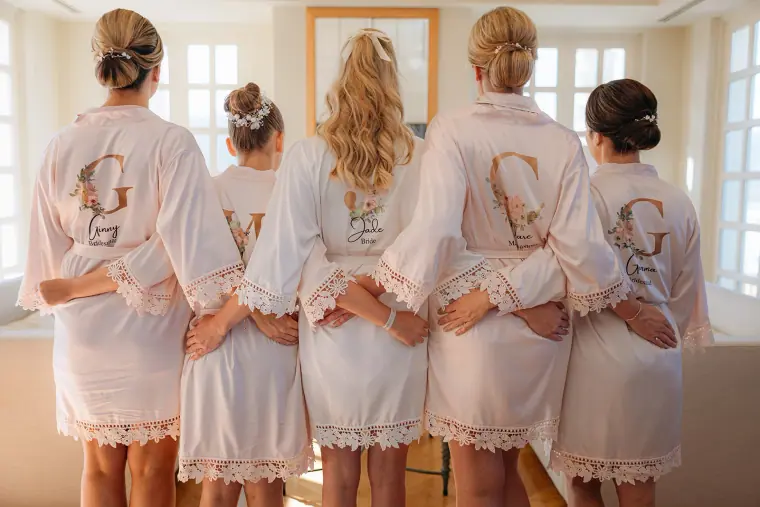Bridesmaids in lace-trimmed monogrammed robes, seen from behind with arms linked