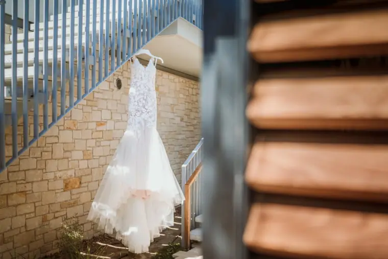 Lace wedding dress hanging from a staircase against a stone wall