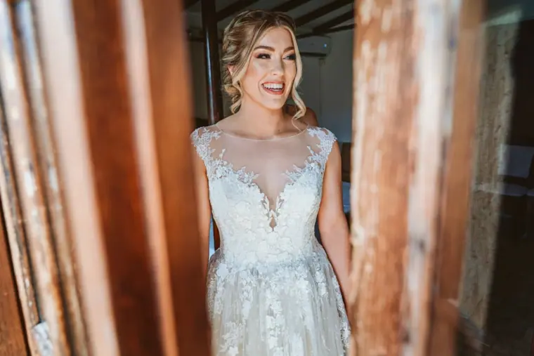 Bride in her lace gown smiling in a rustic wooden doorway