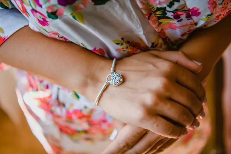 Close-up of the bride's hands and a heart charm bracelet on her floral robe