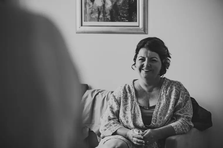 Black-and-white photo of a smiling woman in a patterned jacket sitting in the bridal suite