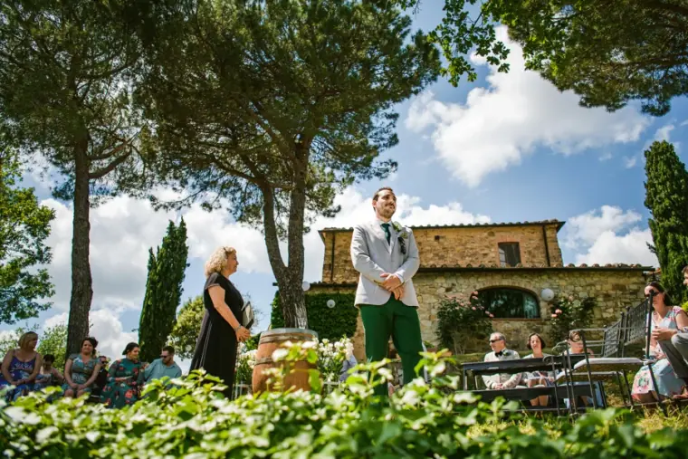 Groom waiting with guests under trees beside the stone villa before the ceremony, Livernano Estate