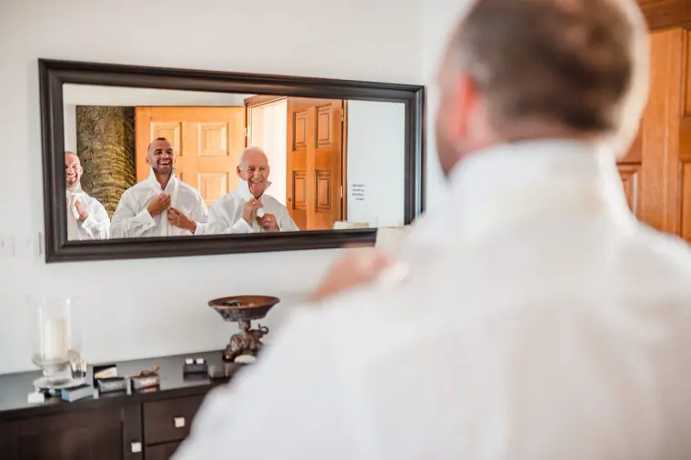 Groom and groomsmen getting ready, reflected in a large mirror