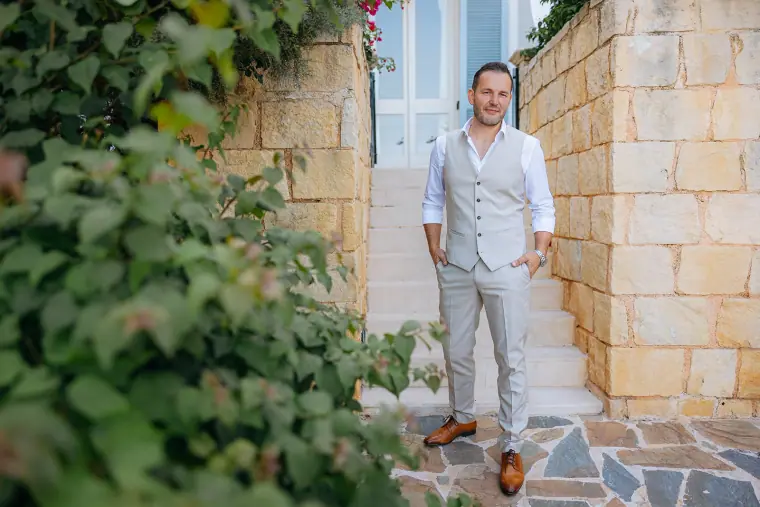 Peter in a beige waistcoat standing on stone steps among bougainvillea