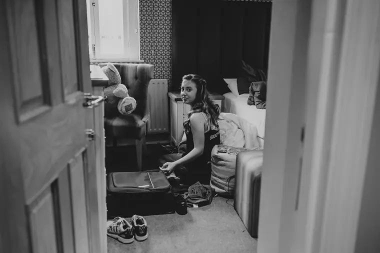 Black-and-white photo of a young bridesmaid sitting on the floor, seen through a door
