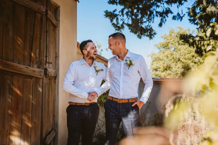 Groom and best man laughing beside a rustic wooden door