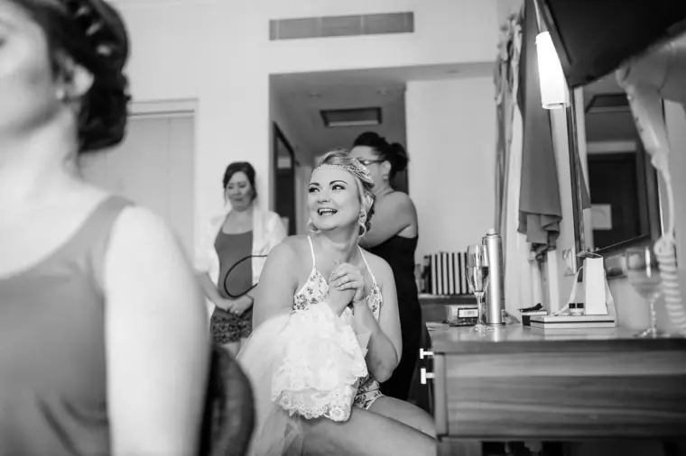Black-and-white photo of the bride laughing as bridesmaids get ready around her