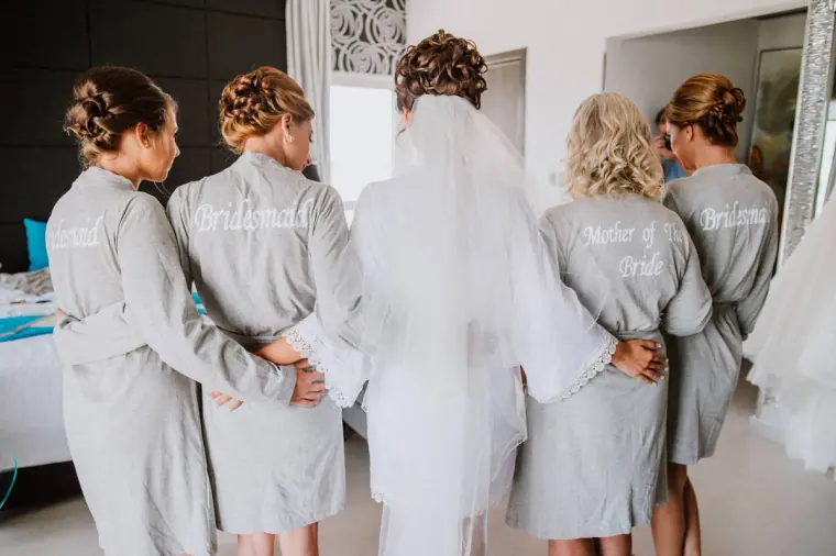 Bridesmaids in matching grey robes with the bride in her veil, seen from behind