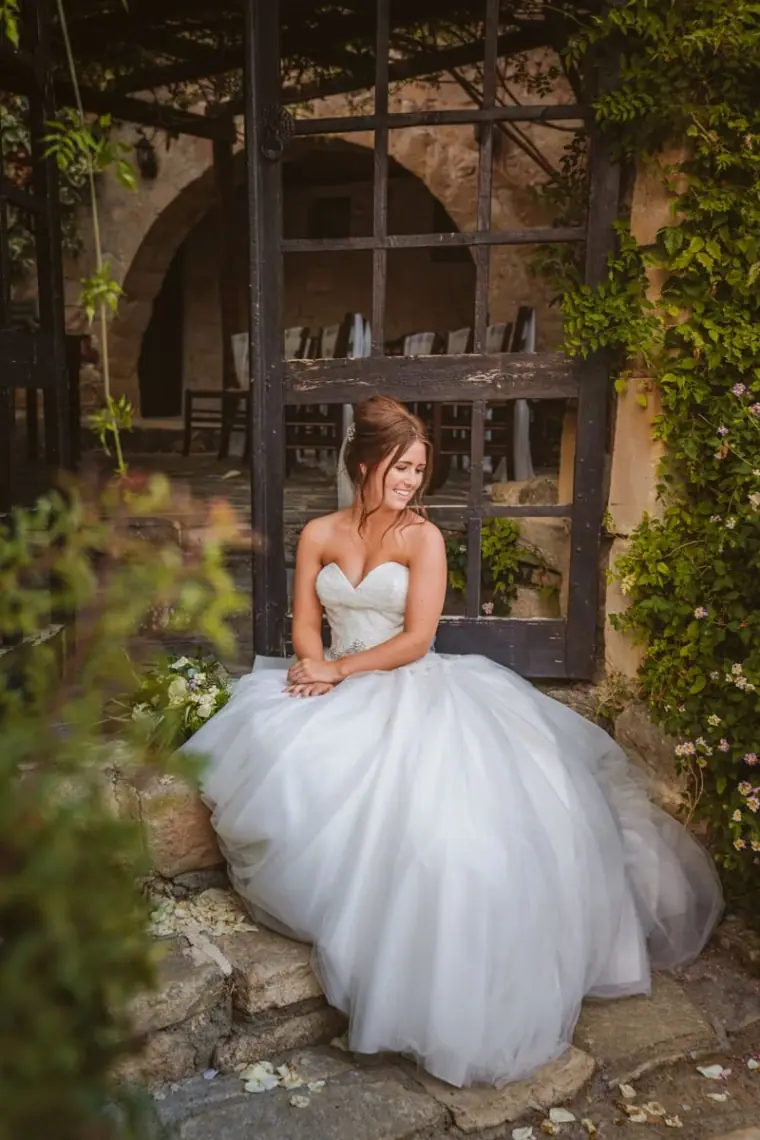 Hannah sitting in her full gown on stone steps beneath a vine-covered pergola