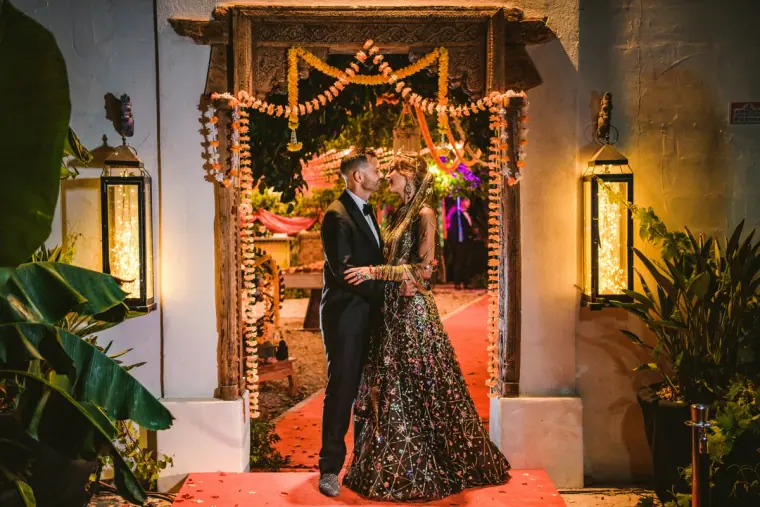Kenton and Hassiba under a marigold-garland archway in embellished evening wear, Ibiza