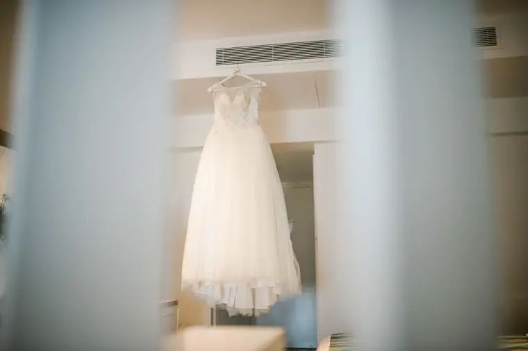 Wedding dress hanging by a white curtain, glimpsed between blurred door frames