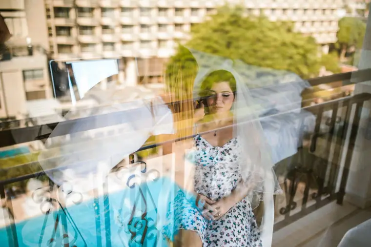 Bride in her veil seen through a window reflecting the hotel pool