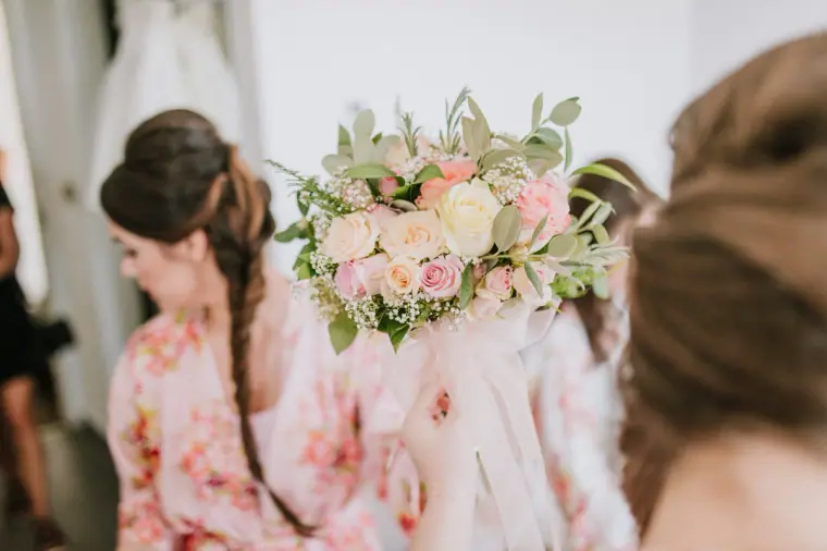 Bridesmaid in a floral robe holding a peach and cream bouquet