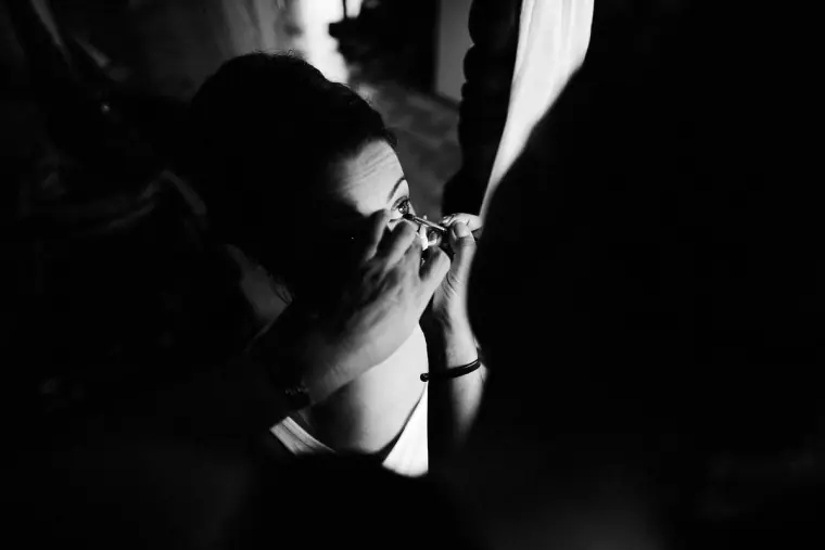 Black-and-white close-up of a woman applying make-up through a curtain