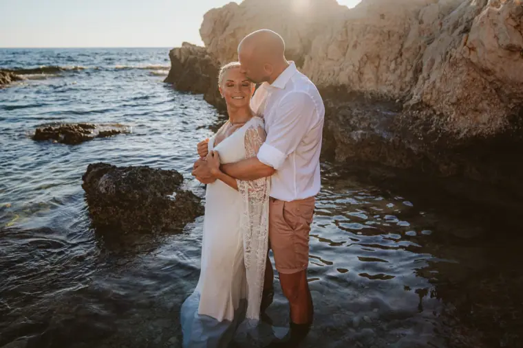 Alana and Luke embracing knee-deep in the water by a rocky outcrop