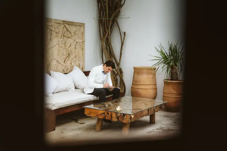 Groom getting ready in a whitewashed lounge, seen through a doorway at Atzaro