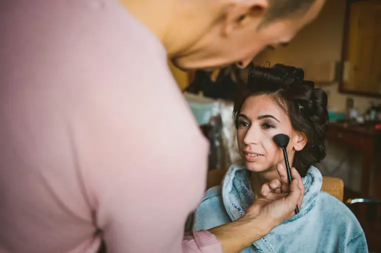 Bride having her make-up brushed on while wearing a blue robe