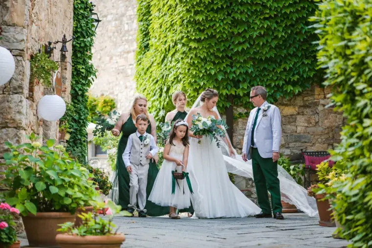 Bride arriving with her father, flower girls and a page boy in an ivy-covered courtyard