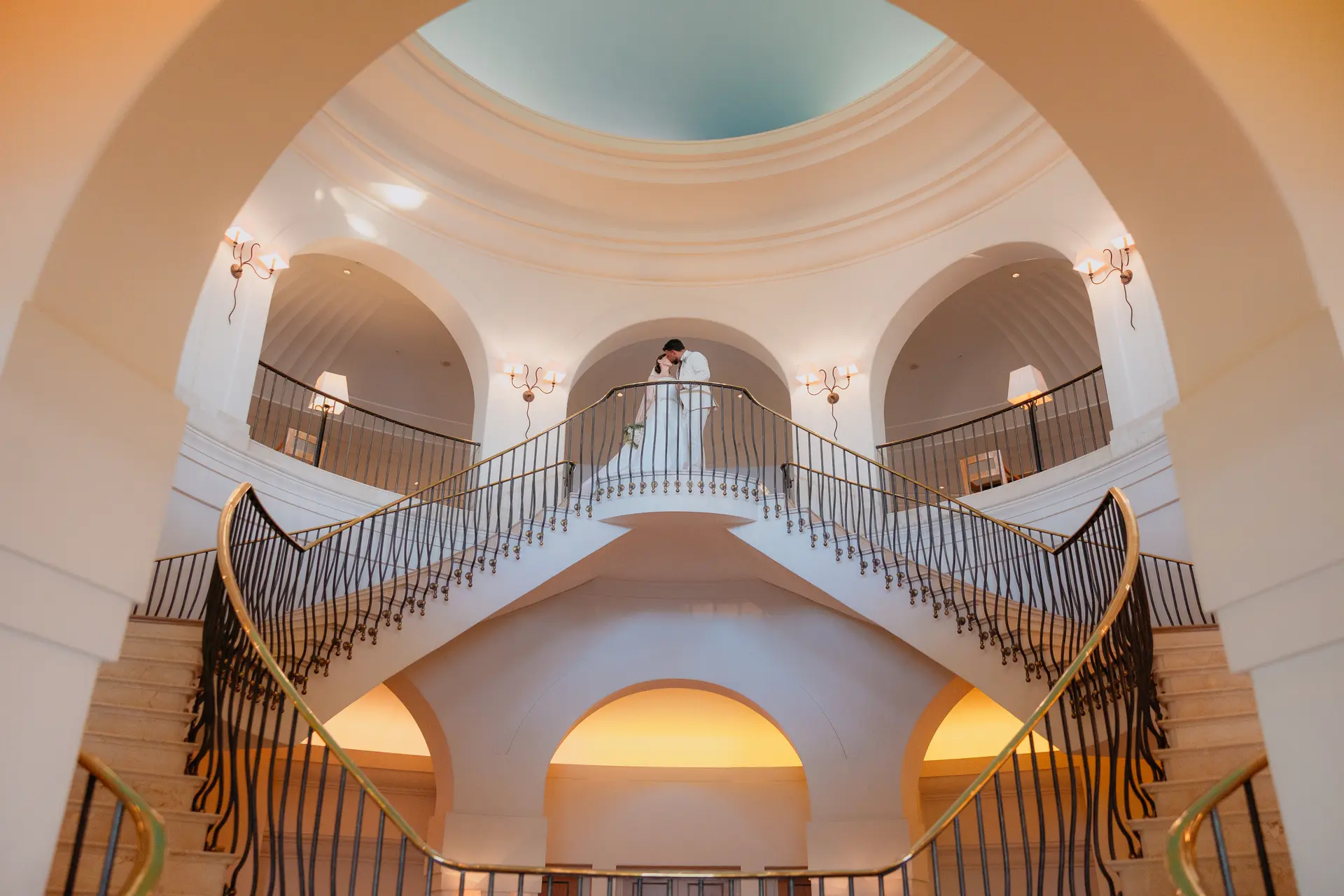 Bride and groom kissing at the top of Anassa's domed double staircase