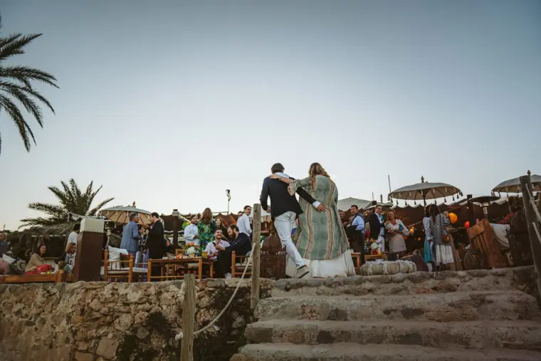 Couple walking down stone steps to the beachfront party with guests waiting below