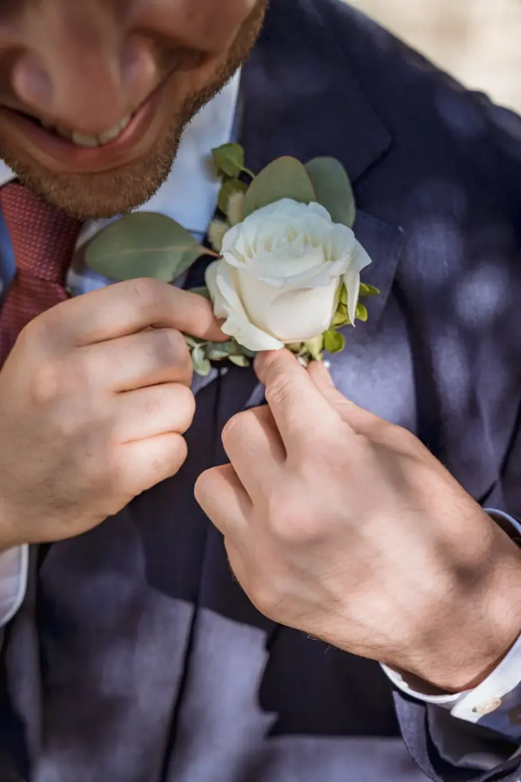 Groom fastening a white rose buttonhole on his navy suit