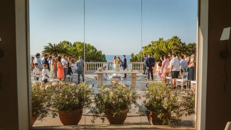 Guests on the terrace watching the ceremony, framed by a doorway, at Anassa Hotel