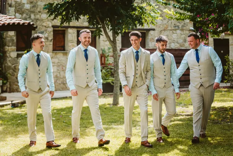 Groom and groomsmen in light waistcoats walking across the lawn at Vasilias Nikoklis Inn