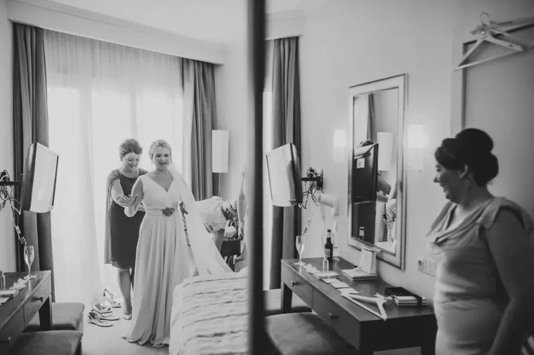 Black-and-white photo of the bride being helped into her dress in the hotel room