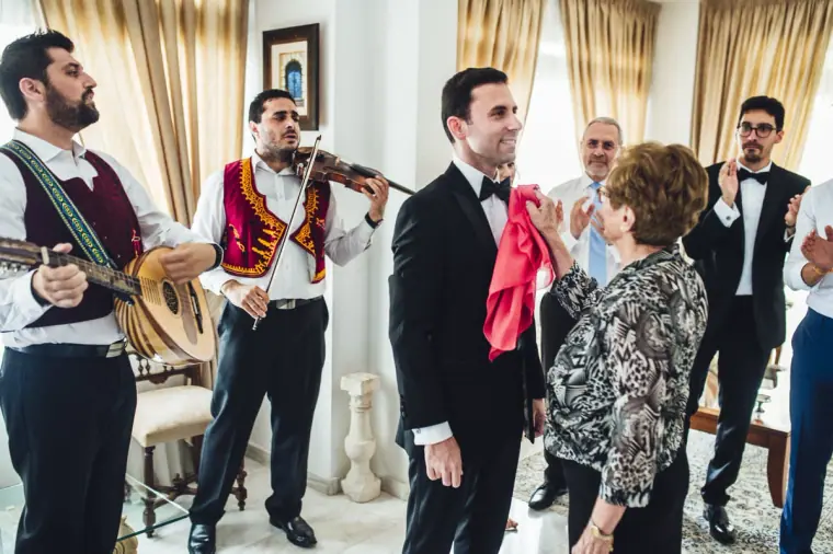Relative tying a red scarf around Angelos as the musicians play