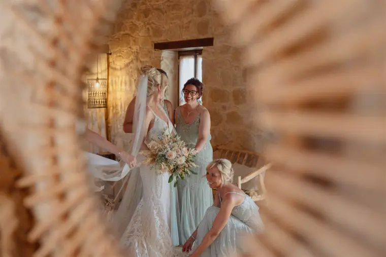 Bride and bridesmaids seen through a rattan sunburst mirror