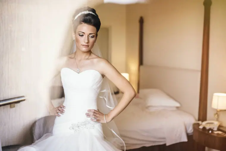 Bride in her strapless gown and veil posing in a hotel bedroom